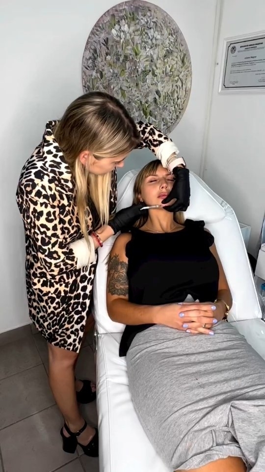 La Dra. Juliana Wagner trabaja sobre los labios de una paciente recostada en la camilla blanca, con el cuadro redondo de hojas en la pared