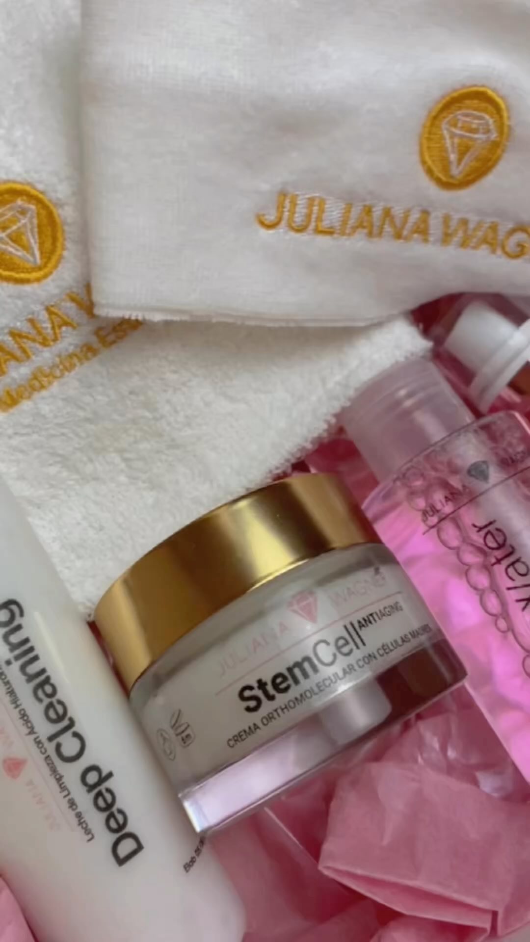Toallas blancas bordadas en dorado con el logo de Juliana Wagner, junto a los productos de su línea: Deep Cleaning y la crema StemCell